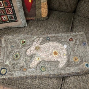 May include: A beige and brown hooked rug with a white rabbit design and colorful circular accents.