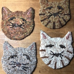 May include: Four handmade cat-shaped rug hookings. The rug hookings are made with different colored yarns and feature a variety of cat faces. The cat faces are all smiling and have black eyes and whiskers.