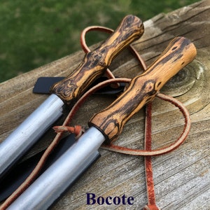 May include: Two fire starters with Bocote wood handles and silver metal strikers. Each has a leather lanyard. The handles display a unique grain pattern with dark brown and tan hues. The text "Bocote" is visible.