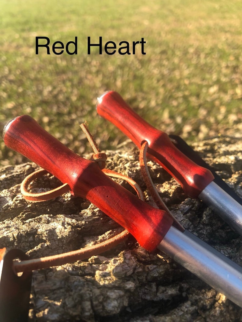 May include: Two red-handled tools with silver shafts, possibly for gardening or crafting, rest on a textured wooden surface. The handles are a deep red, and the text "Red Heart" is visible.
