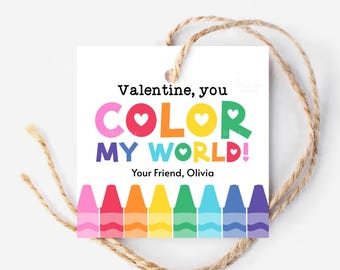 Puede incluir: Una etiqueta de regalo blanca de San Valentín con el texto "Valentine, you COLOR MY WORLD!" en letras coloridas. La etiqueta presenta una fila de crayones en la parte inferior y está atada con una cuerda de hilo natural. La etiqueta está firmada "Your Friend, Olivia."