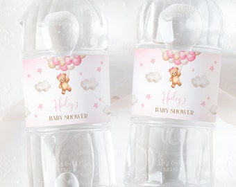 May include: Two clear plastic water bottles with pink and gold labels. The labels feature a cartoon teddy bear holding pink and white balloons, clouds, and stars. The text on the labels reads "Hailey's Baby Shower".