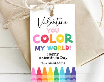 Puede incluir: Una etiqueta de regalo del Día de San Valentín con el mensaje "Valentine, You Color My World!" en letras coloridas. La etiqueta presenta un diseño de crayones en la parte inferior y está atada a un regalo envuelto con hilo. La etiqueta también dice "Feliz Día de San Valentín, Tu amigo/a, Olivia."