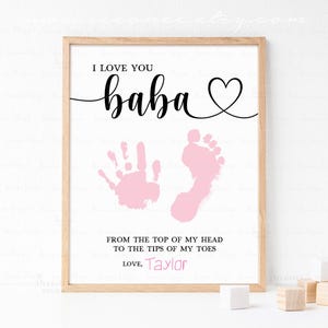 May include: A framed print with the words "I LOVE YOU baba" in black script, a pink handprint and footprint, and the text "FROM THE TOP OF MY HEAD TO THE TIPS OF MY TOES LOVE, Taylor". The print is in a light brown frame.