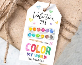 Peut inclure: Une étiquette cadeau blanche avec le texte "Valentine, YOU" et "COLOR MY WORLD!" en lettres colorées. L'étiquette présente une illustration d'une palette de peinture aquarelle et d'un pinceau, avec des cœurs éparpillés. L'étiquette est attachée à un cadeau emballé.