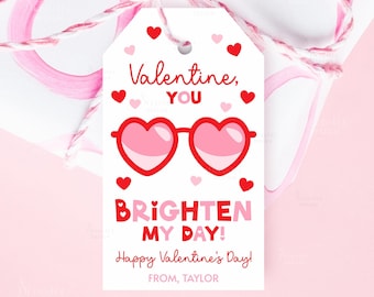 May include: A Valentine's Day gift tag with a white background, featuring red heart-shaped glasses and the text "Valentine, YOU BRIGHTEN MY DAY!" with a pink bow. The tag also says "Happy Valentine's Day!" and "FROM, TAYLOR."