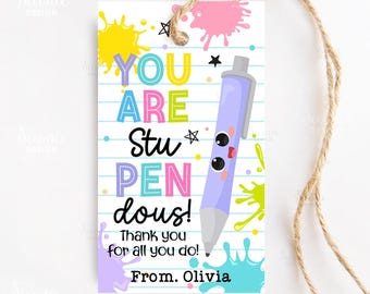 May include: A white gift tag with a lined paper design and a twine string. The tag features colorful text that reads "YOU ARE Stu PEN dous!" with a cartoon pen illustration. Splashes of yellow, pink, and teal paint decorate the tag. The text "Thank you for all you do! From. Olivia" is also present.