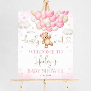 Peut inclure: Une pancarte de bienvenue pour une fête prénatale rose et blanche avec un ours en peluche tenant des ballons. La pancarte indique "We can barely wait" et "Welcome to Hailey's Baby Shower 27.12.2094".
