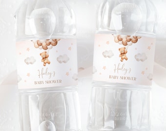 May include: Two clear plastic water bottles with labels featuring a brown teddy bear holding balloons. The labels are pink and white with gold text that reads "Hailey's Baby Shower".