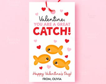 May include: A white Valentine's Day gift tag with a red and white string. The tag features the text "Valentine, YOU ARE A GREAT CATCH!" with three orange cartoon fish and hearts. The tag also says "Happy Valentine's Day! FROM, OLIVIA."