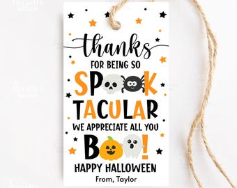 May include: A white Halloween gift tag with a jute string. The tag features the words "thanks" and "Spooktacular" in black and orange, along with a skull, spider, pumpkin, and ghost illustrations. The text "Happy Halloween" is also included.