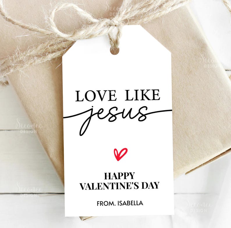 Pode incluir: Uma etiqueta de presente branca com o texto "LOVE LIKE jesus" em preto, com a palavra "jesus" em it&aacute;lico. Abaixo, um cora&ccedil;&atilde;o vermelho e as palavras "HAPPY VALENTINE'S DAY" e "FROM. ISABELLA". A etiqueta est&aacute; amarrada a um presente embrulhado com barbante.