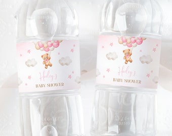 May include: Two clear plastic water bottles with pink and gold labels. The labels feature a cartoon teddy bear holding pink and white balloons, clouds, and stars. The text on the labels reads "Hailey's Baby Shower".
