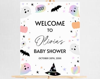 May include: A white baby shower welcome sign with a Halloween theme. The sign features ghosts, bats, pumpkins, stars, and the text "Welcome to Olivia's Baby Shower" with the date October 20th, 20XX.