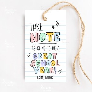 Può includere: Un'etichetta regalo stampabile colorata con il testo "Take Note It's going to be a Great School Year!" con un cuore e stelle. L'etichetta è su uno sfondo bianco con linee blu e il testo "From, Taylor" in basso.