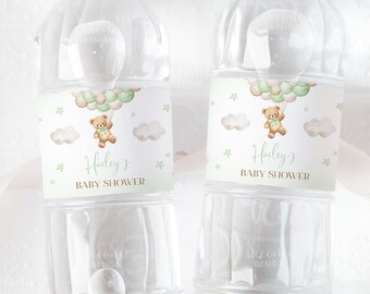 Op de afbeelding: Twee doorzichtige plastic waterflessen met groene, witte en bruine etiketten. De etiketten tonen een cartoonbeer die ballonnen vasthoudt en de tekst "Haley's Baby Shower".