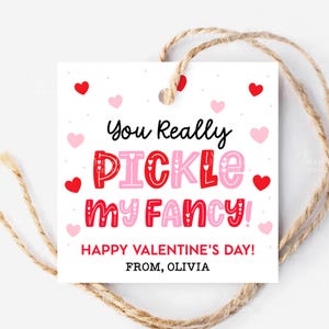 Könnte beinhalten: Ein quadratisches, weißes Valentinstag-Geschenkanhänger mit dem Text "You Really PICKLE my FANCY!" in Rot und Rosa, umgeben von Herzen. Der Anhänger enthält auch den Text "HAPPY VALENTINE'S DAY! FROM, OLIVIA" und ist mit Bindfaden befestigt.