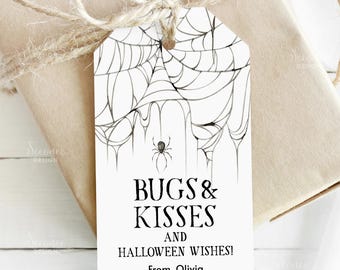 Pode incluir: Uma etiqueta de presente branca de Halloween com um desenho de teia de aranha e uma pequena aranha. A etiqueta diz "BUGS & KISSES AND HALLOWEEN WISHES! From, Olivia." A etiqueta está amarrada a um presente embrulhado.