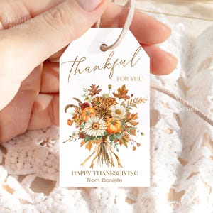 May include: A white gift tag with the words "thankful FOR YOU" in elegant script. The tag features a watercolor bouquet of pumpkins, daisies, and fall foliage. The text "HAPPY THANKSGIVING From, Danielle" is printed below.