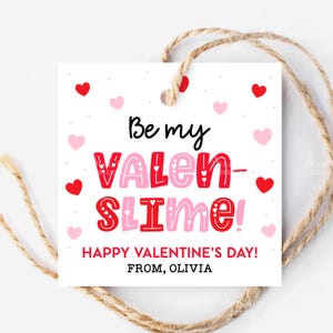May include: A white Valentine's Day gift tag with the text "Be my VALEN-SLIME!" in red and pink, surrounded by red and pink hearts. The tag is tied with a natural twine.