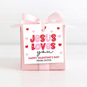 May include: A pink gift box tied with a light pink ribbon and bow. A white tag with red and pink hearts reads "JESUS LOVES you" and "HAPPY VALENTINE'S DAY! FROM, OLIVIA".