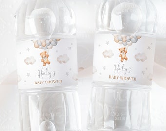 May include: Two clear plastic water bottles with labels featuring a teddy bear holding balloons, clouds, and stars. The labels are white with gold text that reads "Hailey's Baby Shower".