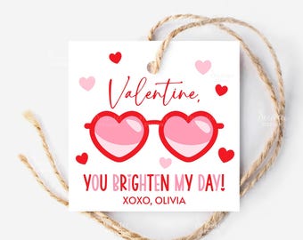 May include: A white Valentine's Day gift tag with red and pink heart-shaped sunglasses and hearts. The tag reads "Valentine, YOU BRIGHTEN MY DAY! XOXO, OLIVIA" and is attached to a natural twine string.