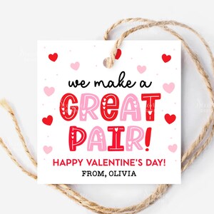 May include: A white Valentine's Day gift tag with the text "we make a GREAT PAIR!" in red and pink. The tag is decorated with red and pink hearts and includes the message "HAPPY VALENTINE'S DAY!" and "FROM, OLIVIA". A natural twine string is attached.