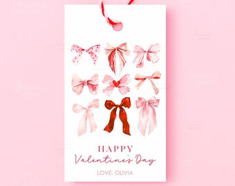 May include: A white gift tag with watercolor illustrations of bows in shades of pink and red. The tag reads "Happy Valentine's Day" and "Love, Olivia" in red script, with a red and white string.
