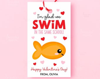 May include: A white gift tag with a red and white string. The tag features the text "I'm glad we SWIM in the same school!" in red and black. A cartoon orange fish and hearts decorate the tag. The text "Happy Valentine's Day!" and "FROM, OLIVIA" are also present.