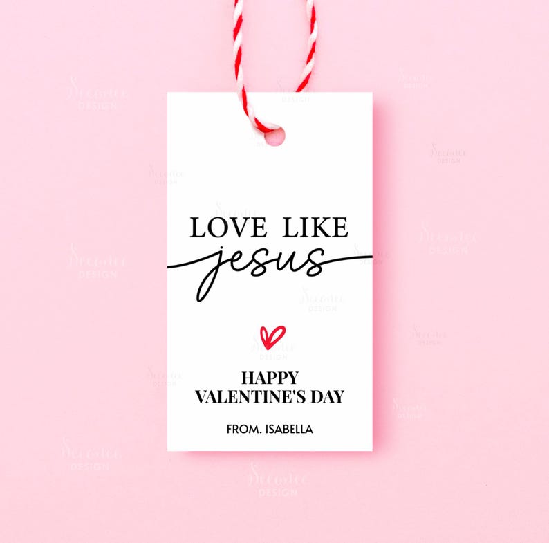Pode incluir: Uma etiqueta de presente branca com o texto "LOVE LIKE jesus" em escrita preta, um pequeno cora&ccedil;&atilde;o vermelho e "HAPPY VALENTINE'S DAY" abaixo. A etiqueta est&aacute; presa a uma corda vermelha e branca, em um fundo rosa.
