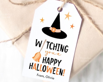 Op de afbeelding: Witte Halloween-cadeaulabel met een zwarte heksenhoed, oranje sterren en de tekst "Watching you a Happy Halloween!" met een bezemafbeelding. Het label is met touw aan een ingepakt cadeau bevestigd.