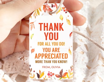 May include: A white gift tag with the words "THANK YOU" in orange, surrounded by autumn leaves. The tag also includes the phrases "FOR ALL YOU DO!" and "YOU ARE APPRECIATED". A tan string is attached.
