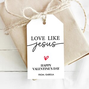 Pode incluir: Uma etiqueta de presente branca com o texto "LOVE LIKE Jesus" em escrita preta e um cora&ccedil;&atilde;o vermelho. Abaixo, l&ecirc;-se "HAPPY VALENTINE'S DAY" e "FROM. ISABELLA". A etiqueta est&aacute; amarrada a um presente embrulhado com barbante.