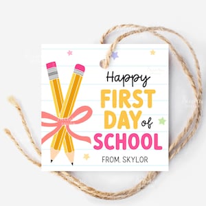 May include: A square gift tag with a school theme. The tag features two yellow pencils, a pink bow, and the text "Happy FIRST DAY of SCHOOL" in black, yellow, and pink. The tag is tied with a natural twine.