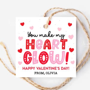 May include: A white Valentine's Day gift tag with a jute string. The tag features the text "You make my HEART GLOW! HAPPY VALENTINE'S DAY! FROM, OLIVIA" in red and pink, with heart accents.