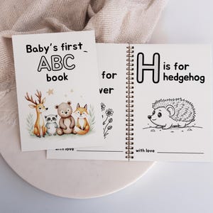 May include: A black and white illustrated alphabet book for babies. The cover features the letters ABC and the words "Baby's first ABC book". The inside page shows the letter H and the words "H is for hedgehog" with a black and white illustration of a hedgehog.