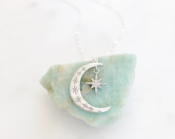 May include: A silver necklace with a crescent moon pendant and a dangling star charm. The star is encrusted with small, clear stones.