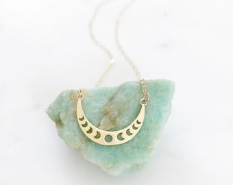 May include: A gold necklace with a crescent moon pendant featuring a cutout design of multiple moon phases.
