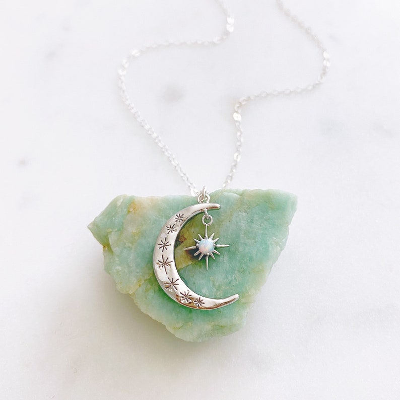 K&ouml;nnte beinhalten: Eine silberne Halskette mit einem Halbmond-Anh&auml;nger und einem Stern-Anh&auml;nger mit einem Opal-Stein. Die Halskette liegt auf einem gr&uuml;nen Steinuntergrund.