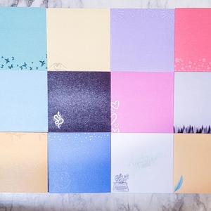 May include: A collection of twelve square notepads in various pastel colors, including blue, pink, and beige. Each notepad features a different decorative design, such as butterflies, hearts, and floral patterns. Some pads have text, including the phrase "Special Delivery".