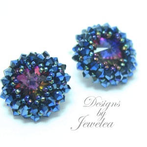 Puede incluir: Un par de pendientes azul y morado iridiscentes con un centro de cristal. Los pendientes están hechos de pequeñas cuentas y tienen un diseño de flor.