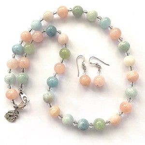 May include: A pastel-colored beaded necklace and matching earrings set. The necklace and earrings feature round, polished beads in shades of pink, green, and blue, interspersed with clear crystal accents. The necklace has a silver clasp.