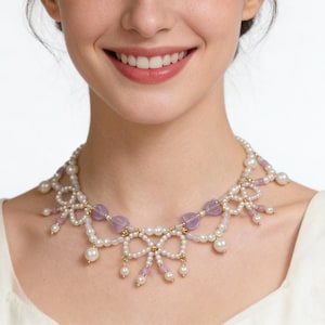 Op de afbeelding: Een delicate ketting met witte parels, lavendelkleurige kralen en goudkleurige accenten. De ketting heeft een strikvormig ontwerp met bungelende pareldruppels. De vrouw op de foto draagt een crèmekleurige top.