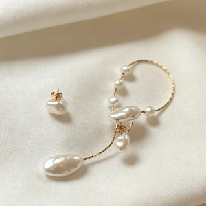Può includere: Un paio di orecchini color oro con perle bianche irregolari. Un orecchino è un semplice bottone con una perla, l'altro è un orecchino con una sottile catenina dorata, diverse piccole perle rotonde e due perle più grandi.