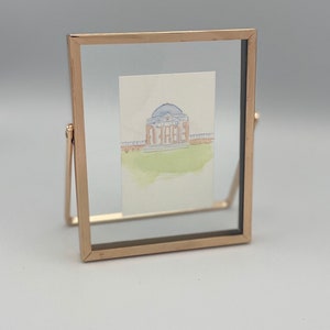 May include: A watercolor painting of a building with a dome, framed in a gold metal frame. The painting is on a white background and the frame is on a white surface.