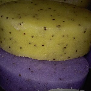 May include: Two bath scrub bars, one is purple and one is yellow. Both bars have small black seeds embedded in them.