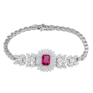 May include: A silver bracelet with a central rectangular ruby and white gemstones. The bracelet has a floral design with leaf-shaped accents and a clasp. A piece of elegant jewellery.