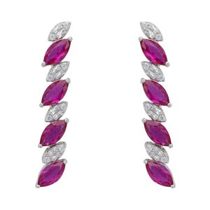 Op de afbeelding: Een paar elegante oorbellen met afwisselend marquise-geslepen, fuchsia-kleurige edelstenen en kleinere, heldere edelstenen. De oorbellen zijn gezet in een zilverkleurig metaal en worden getoond tegen een witte achtergrond.