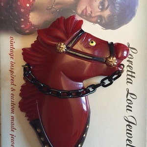 Op de afbeelding: Een rode plastic paardenkop broche met een zwarte ketting en gouden accenten. De broche is op een witte achtergrond met de tekst "Loretta Lou Jewels" en "vintage inspired & custom made jewelry".
